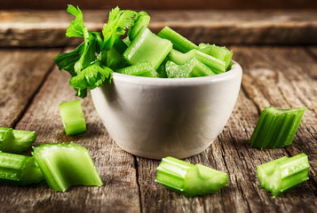Fresh sliced celery in a white bowl on a vintage wooden background, selective focus