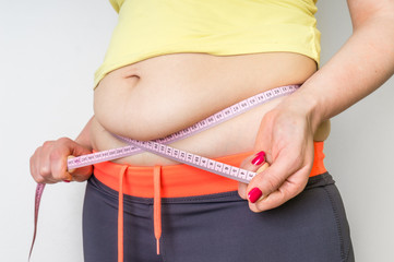 Overweight woman with tape is measuring fat on belly