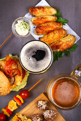 Glasses of beer with chicken wings, burger, meat balls, grilled corn and vegetables. Beer bites. Ale and food still life. View from above, top studio shot