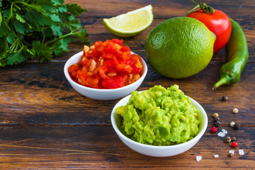 Homemade salsa and guacamole sauces in small white bowls on the wooden rustic table.