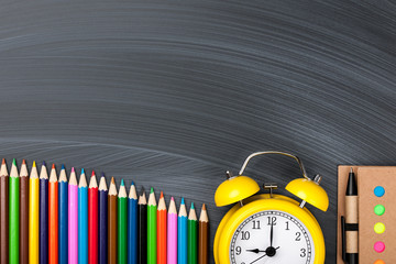 Colorful pencils, alarm clock and notepad on blackboard