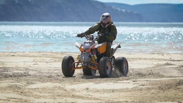 A man with a helmet on his head rides along a sandy beach near the sea on a sport ATV, a person quickly turns the vehicle with a rudder on a vehicle