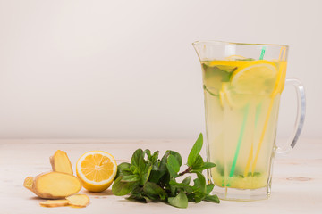 A glass decanter with a summer refreshing lemonade made of lemons and ginger with mint added on a...