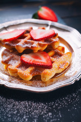Homemade classic Belgian waffles topped with fresh strawberry and powdered sugar on vintage plate