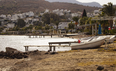 View of empty beach, small piers and white small boat at Turkbuku village in Bodrum peninsula in autumn. The image also shows how tourism crises effects the region.