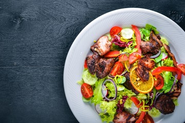 Salad with fresh cucumbers, tomatoes and greens with grilled meat on a plate Wooden board. Top view. Free space.