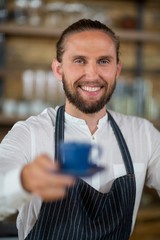 Portrait of smiling waiter offering cup of coffee