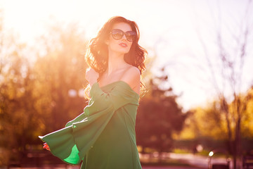 Beautiful Fashion elegant woman posing in summer garden in trendy green dress and sunglasses.