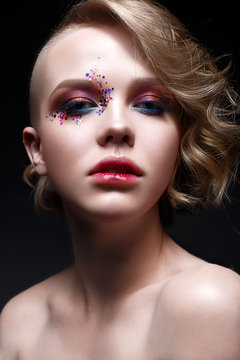 A young girl with a short haircut and bright creative makeup. A beautiful model with sparkles on the face and red lips. Evening makeup, beauty of the face. Photo is taken in a studio.