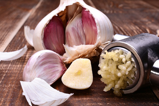 Sliced garlic, garlic clove, garlic bulb and garlic press on wooden table.