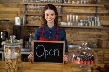 Smiling waitress showing chalkboard with open sign at counter