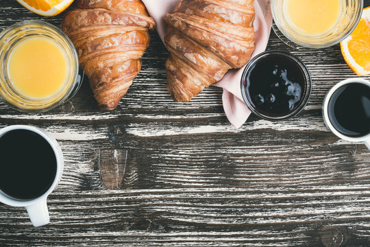Croissants with coffee cup and orange juice on a wooden table, top view