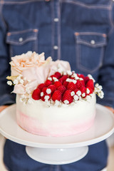 Woman holding sweet white cream mousse cake with raspberries on cake stand