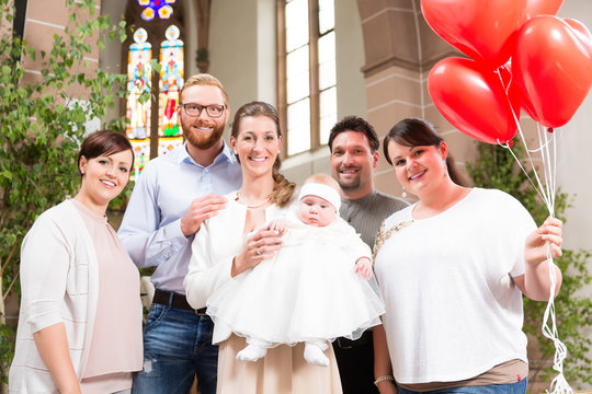 Familie mit Baby nach der Taufe vor dem Altar mit roten Luftballons
