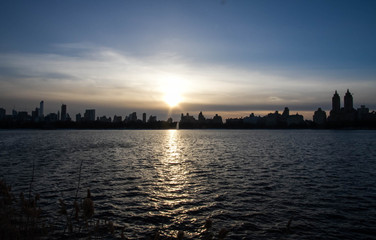 Silhouette buildings in Manhattan with blue sunset sky and reflective lake
