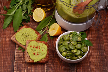 Toast with bean paste and boiled broad beans on wooden background.