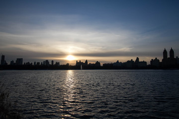 Sunset over silhouette buildings and lake with blue sky