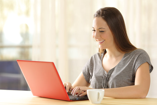 Girl typing in a red laptop at home