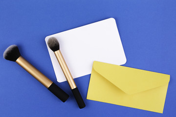 Make up brushes and yellow envelope with blank card on blue background