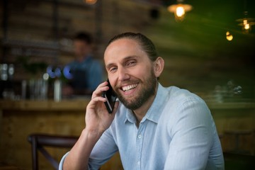 Smiling man talking on mobile phone at café