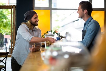 Smiling waiter serving cup of coffee to man at counter 