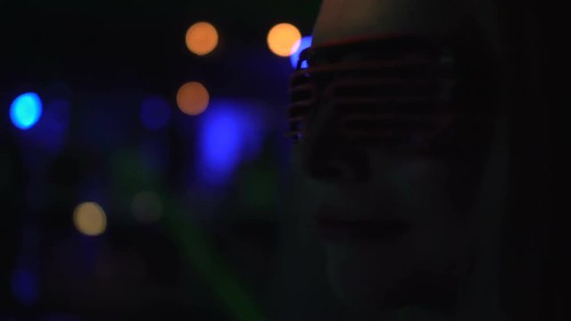 Closeup side face of pretty woman in pink leg glasses dancing at the party over disco lights background