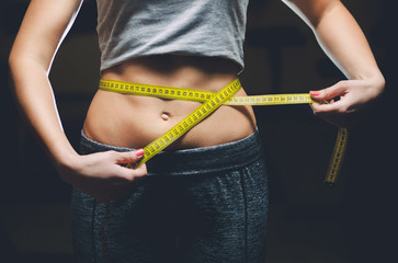Slim girl bodybuilder centimeter measuring her waist in a gym. Sports concept, fat burning and a healthy lifestyle.