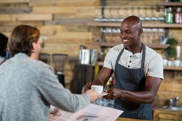 Waiter serving cup of coffee to man at counter