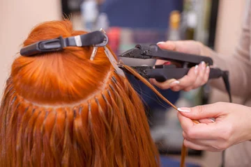 Crédence de cuisine en verre imprimé Salon de coiffure The hairdresser does hair extensions to a young, red-haired girl, in a beauty salon. Professional hair care.