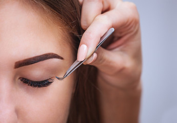 Makeup Master corrects, and strengthens eyelashes beams, holding out a pair of tweezers in a beauty salon. Professional care for the skin and eyes.