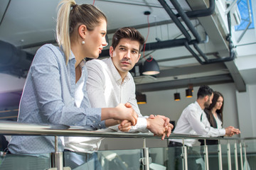 Business colleagues talking while they are leaning on the railing of the balcony in the office building.