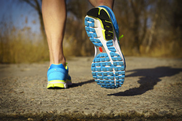 Back view of male muscular feet in sneakers walking on sidewalk in spring sunny day