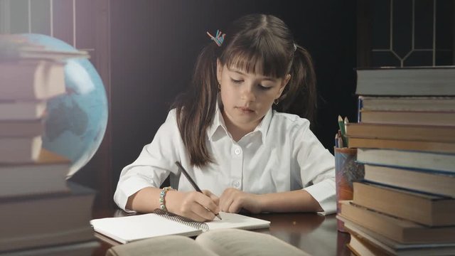 Eight years school girl writing in her notebook, studying place with books and globe, education concept, 30FPS