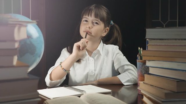 Eight years thoughtful school girl writing in her notebook, studying place with books and globe, education concept, 30FPS