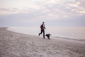 young man run and playing with black dog on the beach