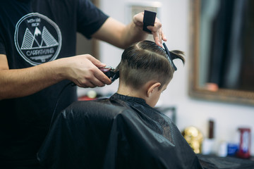 Little boy on a haircut in the barber sits on a chair.