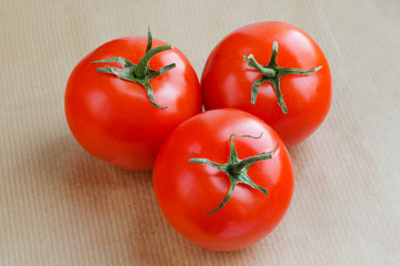 Three red tomatoes on the light beige paper