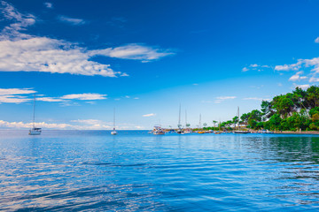 Fototapeta na wymiar Wonderful romantic summer landscape panorama coastline sea. Boats and yachts in harbor at cristal clear azure water. Green trees at the edge of the coast.