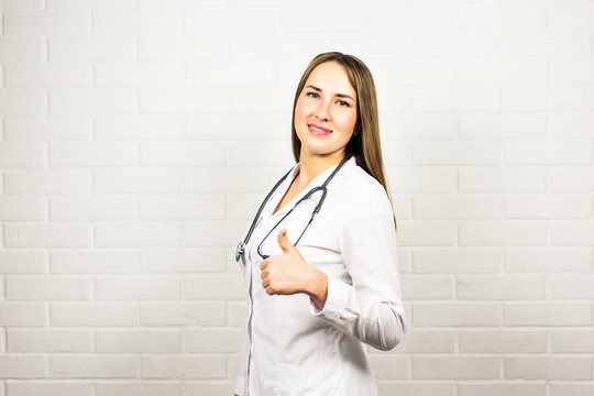 Happy smiling female doctor showing thumbs up hand sign gesture, at office, with blank copyspace area for slogan or advertise text. Healthcare, medical, lab consulting and exam concept.