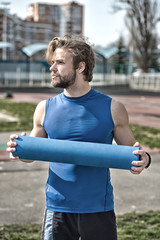 man with muscular body, beard holding yoga or fitness mat