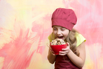 small girl in red chef hat, apron with chocolate cookies