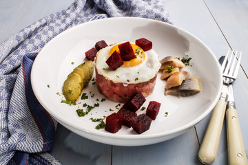 labskaus, north german specialty made with potatoes, beetroot, sour herring, gherkin slices, fried egg and parsley on a plate