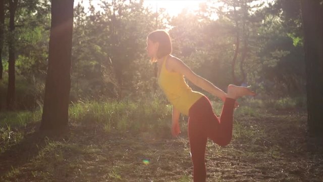 Girl practicing yoga stretching at sunset in forest. Slow motion steadicam shot