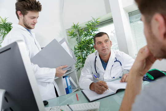 Doctor in consultation with patient, student doctor holding notes