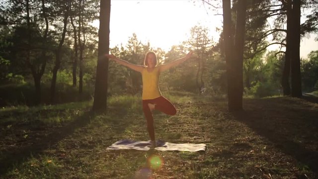 Girl practicing yoga stretching at sunset in forest. Slow motion Vrksasana pose