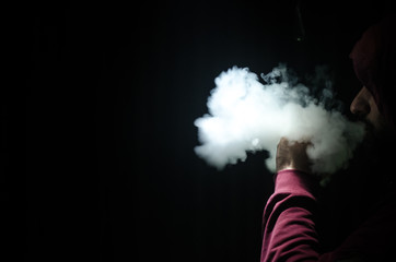 Vaping man holding a mod. A cloud of vapor. Black background. Vaping an electronic cigarette with a...
