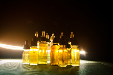 Vape concept. Smoke clouds and vape liquid bottles on dark background. Light effects.
