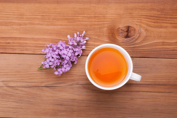 Cup of tea and lilac flowers on a wooden background.