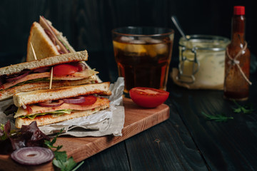 Fresh delicious club sandwich, sauces and drink on the wooden dark table