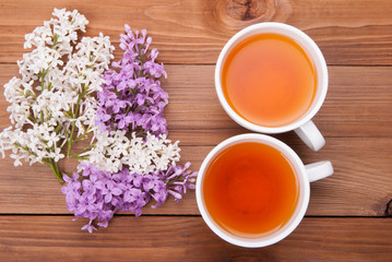 Two cups of tea and lilac flowers on a wooden background.